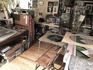The artist's studio full of in-progress stained glass work, materials, and inspirational items and past artwork on the walls