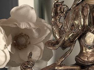 the hands of a Buddha shrine statue and a white flower behind it