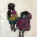 two children standing in the snow laughing with their coats on backwards, the one on the left in a rainbow striped coat, facing away with hood up and pony tail hanging out the front, the one on the right in a pink coat facing the viewer laughing with hair blowing across her eyes and hood hanging down loosely under her chin