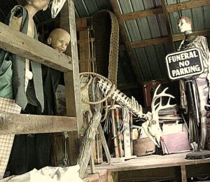 rustic old items like broken mannequins dressed in vintage clothing, records, a funeral parking sign, and a deer skeleton gathered in a barn loft